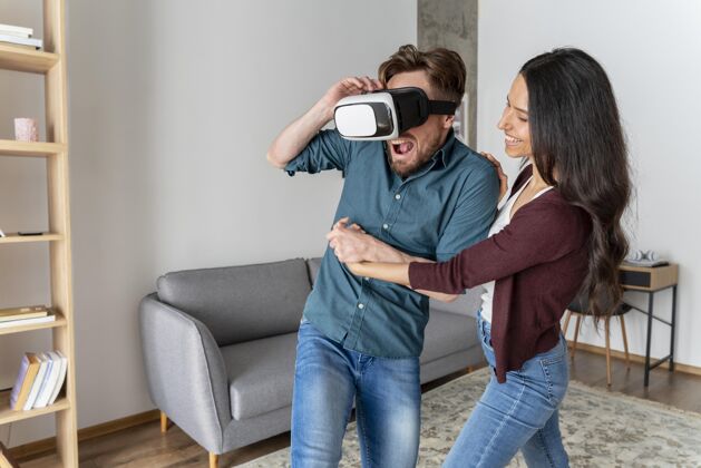 娱乐男人在家里玩虚拟现实耳机旁边的女人男人女人虚拟现实眼镜