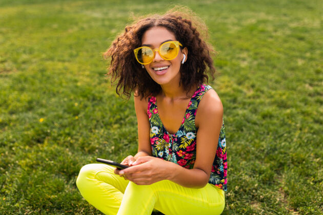 音乐年轻时尚微笑的黑人女子使用智能手机 通过无线耳机听音乐 在公园里玩得很开心眼镜女孩兴奋