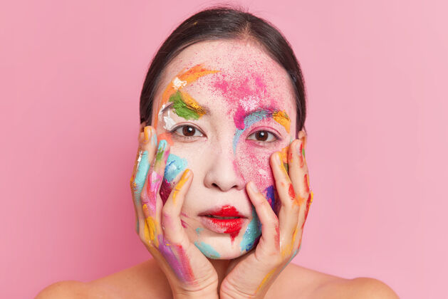 绘画美丽的亚洲年轻女子双手放在脸颊上 脸上涂着五颜六色的颜料肖像设计封面