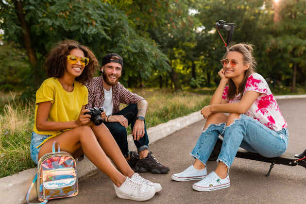 街道快乐的年轻朋友们坐在公园的草地上 带着电动脚踏车微笑着 男女同乐女士酷女孩
