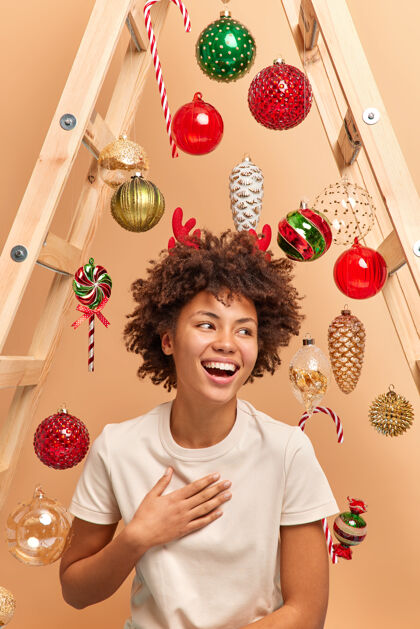 圣诞节室内拍摄的美丽微笑的年轻女子 卷曲的非洲头发 开心地笑着 一边看一边穿着红鹿角休闲白色t恤快乐地过寒假准备在家过圣诞节女人女人节日