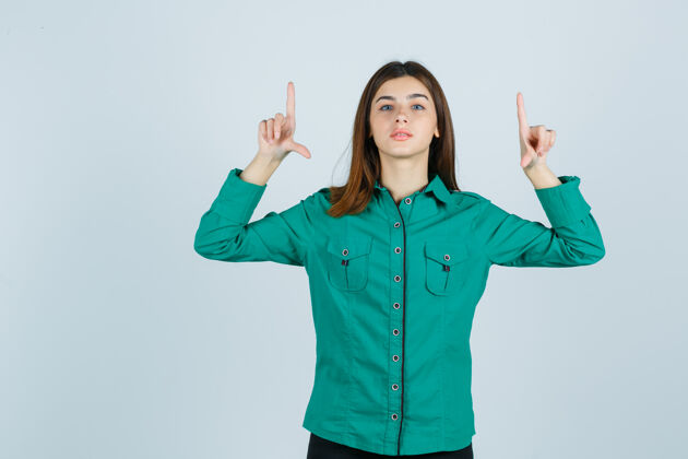 欢呼年轻的女性指着绿色衬衫 看起来很自信 正面视图时尚办公室微笑