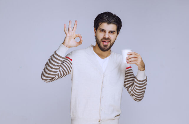 年轻一个穿着白衬衫的男人拿着一个咖啡杯 做着一个好手势人体模特摄影人