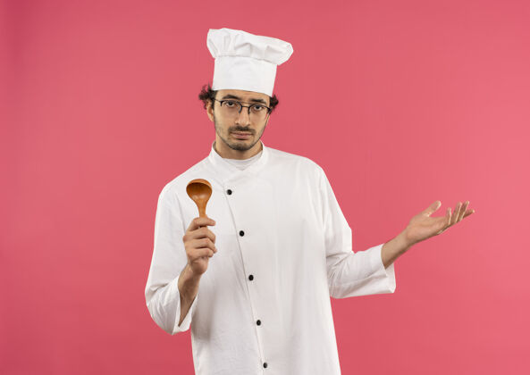 拿着年轻的男厨师穿着厨师制服 戴着眼镜 手里拿着勺子 摊开了手烹饪厨师勺子