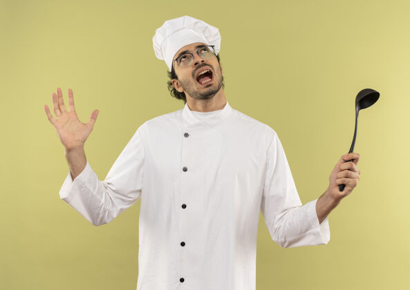 眼镜看着怒气冲冲的年轻男厨师 穿着厨师制服 戴着眼镜 手里拿着勺子 摊开了手烹饪愤怒绿