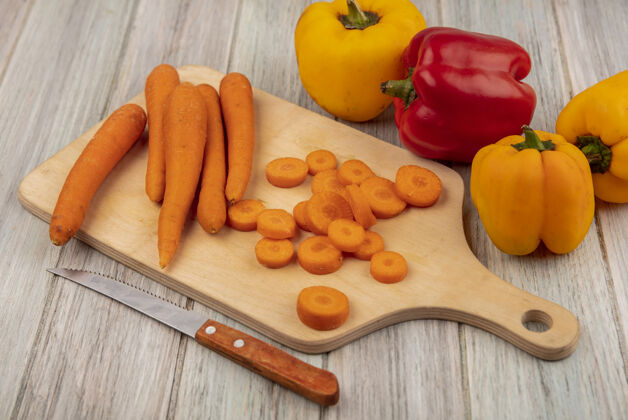 厨房顶视图丰富的维生素和矿物质蔬菜胡萝卜在一个木制的厨房板上与彩色甜椒刀隔离在一个灰色的木制表面一餐胡萝卜营养