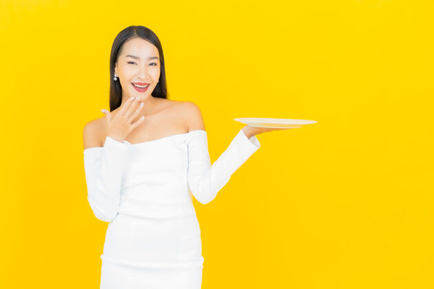 甜点美丽的亚洲商界年轻女子的画像 黄色墙上有空盘子快乐成人员工