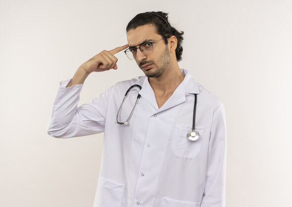 医生自信的年轻男医生戴着眼镜 穿着白色长袍 听诊器把手指放在额头上眼镜男人眼镜
