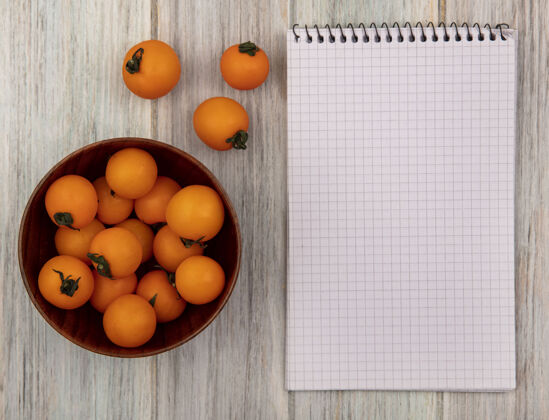 健康新鲜的橙色樱桃西红柿的顶视图在一个灰色的木制表面与复制空间的木碗新鲜樱桃配料
