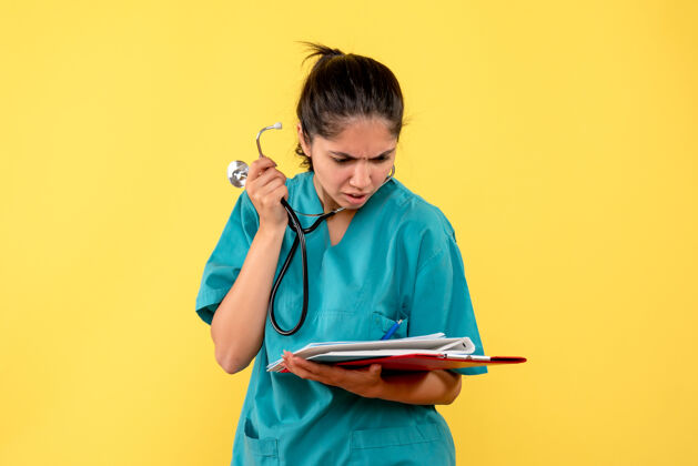 纸张穿着制服的女医生正看着黄色墙上的文件器械医疗器械正面