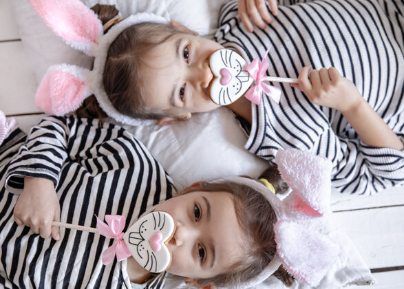 年轻可爱的小姐妹们 带着复活节姜饼 兔子脸和兔子耳朵举行顶视图棒