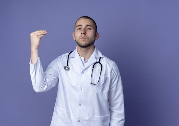 医疗自信的年轻男性医生 穿着医用长袍 脖子上戴着听诊器 假装拿着什么东西 在紫色的空间里显得孤立长袍医生男性