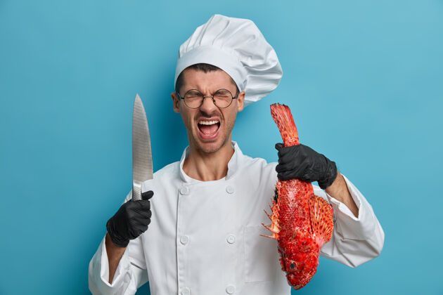 食物专业的法国厨师在厨房里花了很多时间 穿着制服 戴着黑色橡胶手套 摆着鱼和刀的姿势海鲜鱼室内