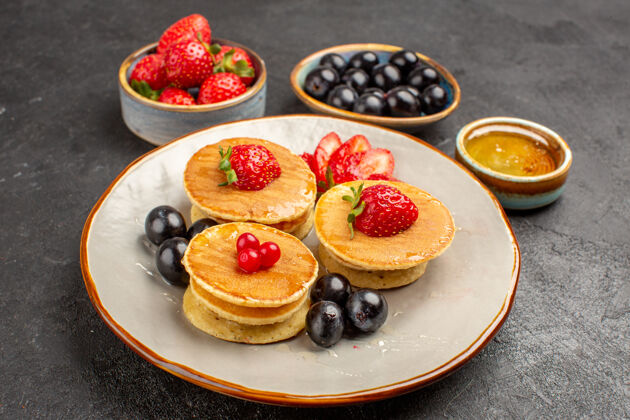 早餐正面图美味的薄煎饼 灰色表面上有水果馅饼水果蛋糕盘子小草莓