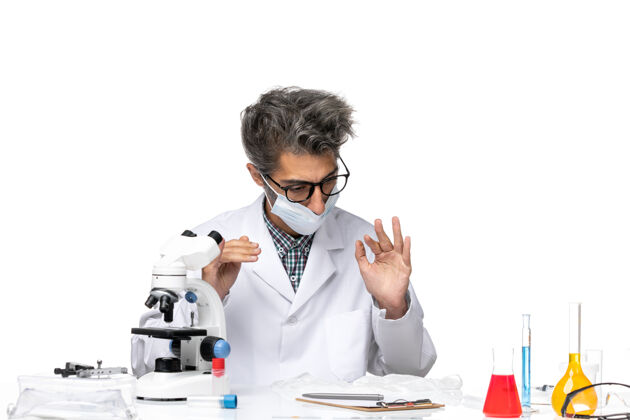 特殊正面图中年科学家穿着特制的西装 戴着面具围坐在桌子旁 拿着解决方案周围实验室外套