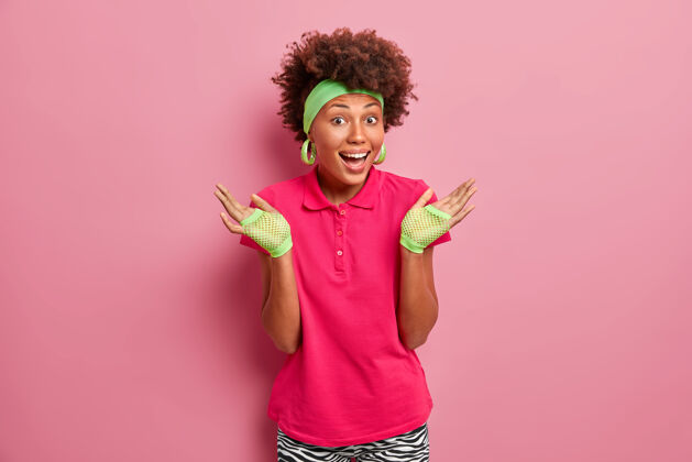 美国快乐的女人 自然卷发 举手 困惑 开怀大笑 戴运动手套 亮粉色t恤 在室内摆姿势魅力心情非洲