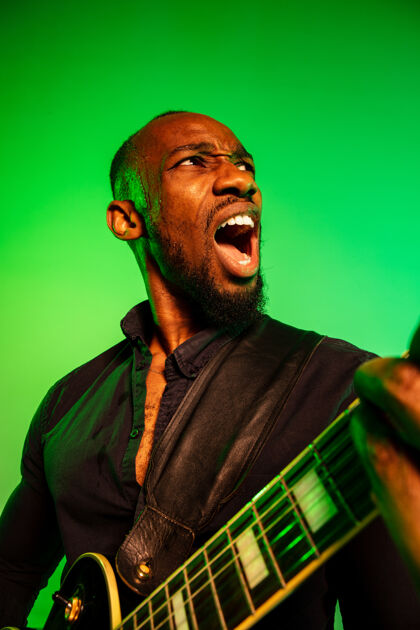 表演年轻的非洲裔美国音乐家 在渐变的绿黄色背景下像摇滚明星一样弹吉他成人露天日