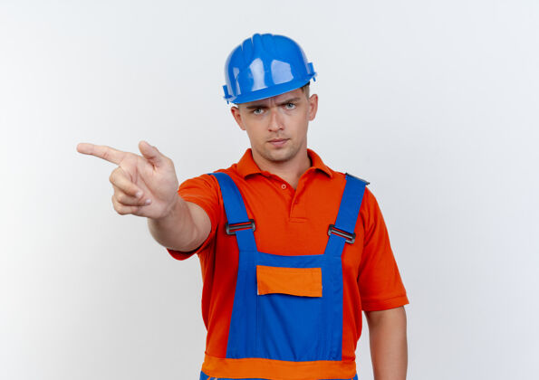 年轻严格年轻的男建筑工人穿着制服 安全帽点在白色边上壁板空间建设者