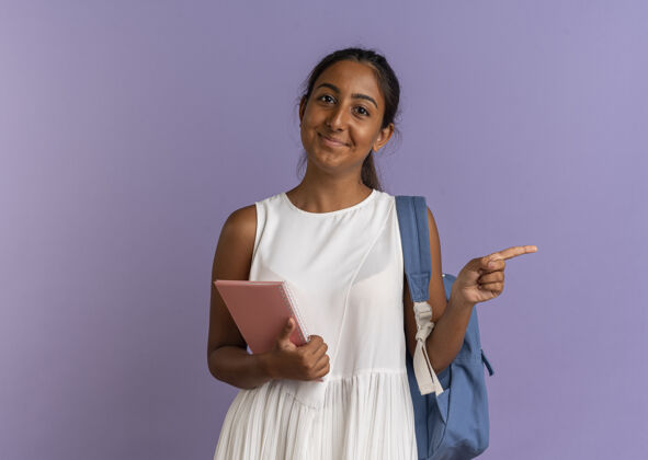 拿着高兴的小女生背着书包拿着笔记本 指着边上的紫色笔记本包女学生