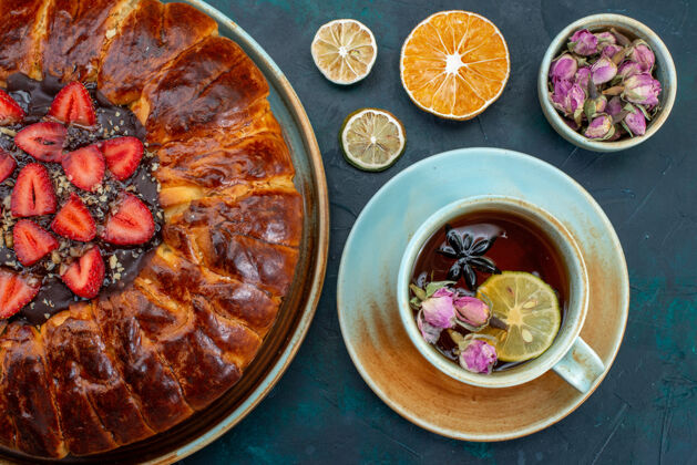 盘子俯瞰美味的草莓派 深蓝色的表面上放着一杯茶 烤着美味的蛋糕糖草莓烘焙的