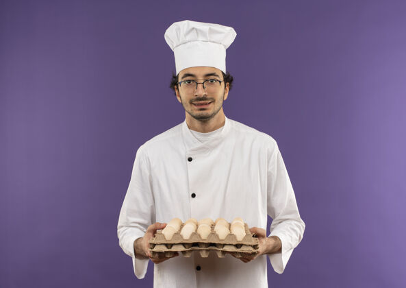 眼镜高兴的年轻男厨师穿着厨师制服 戴着一副紫色的眼镜 手里拿着一批鸡蛋持有烹饪紫色