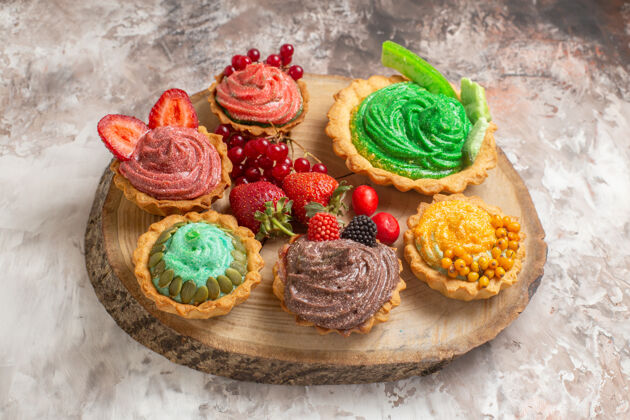 糖果正面图：美味的奶油蛋糕和水果放在浅色的桌子上甜点饼干甜蛋糕美味食品糖果