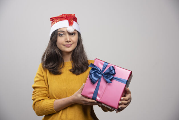 女孩带着圣诞礼物的戴着圣诞老人红帽子的微笑女人礼品盒帽子圣诞老人