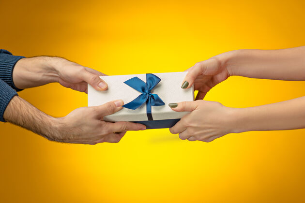 盒子特写图片的男人和女人的手与礼品盒的黄色背景事件惊喜包装