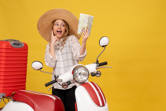 年轻女子俯视图：戴着帽子 坐在摩托车上拿着地图 正在收行李的快乐微笑的年轻女子行李摩托车人