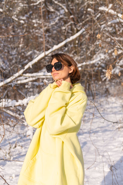 旅行阳光明媚的日子里 雪景冬林中一位年轻美女的画像 身着黄色大套头衫 戴着墨镜 享受着阳光和雪快乐森林白牙