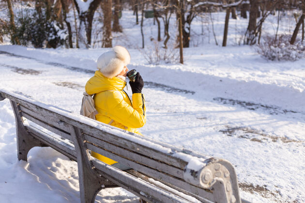 咖啡冬天的快乐年轻女子 穿着暖和的衣服 在阳光明媚的日子里 坐在长椅上 独自享受着新鲜的空气和咖啡快乐冬天的衣服杯子