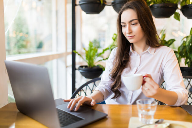 设备美丽的白种女人坐在现代的咖啡吧里 手里拿着一本便携的上网本 梦想着什么年轻迷人的女性自由职业者 在笔记本电脑上工作时思考着新的想法女性学生人