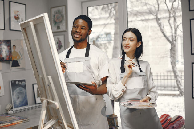 学生一个非洲男人和一个女人在画架上画画围裙室内画笔