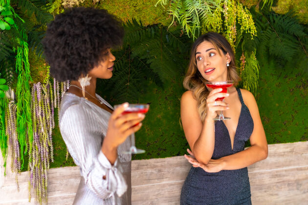饮酒非裔美国人和白人女性朋友穿着花哨的衣服喝酒聊天时尚女性白种人