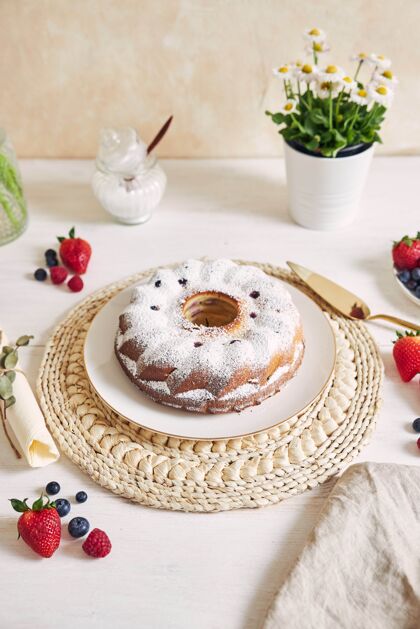 烘焙垂直拍摄的一个环形蛋糕与水果和粉末上的白色桌子与白色鲜花圆形糕点