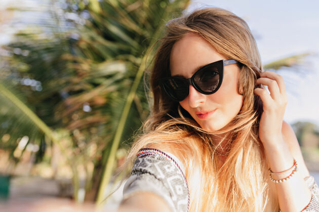 放松美丽的白种女人在沙滩上与棕榈树自拍戴着黑色太阳镜的迷人女孩在异国他乡度假的户外照片欢乐背景度假