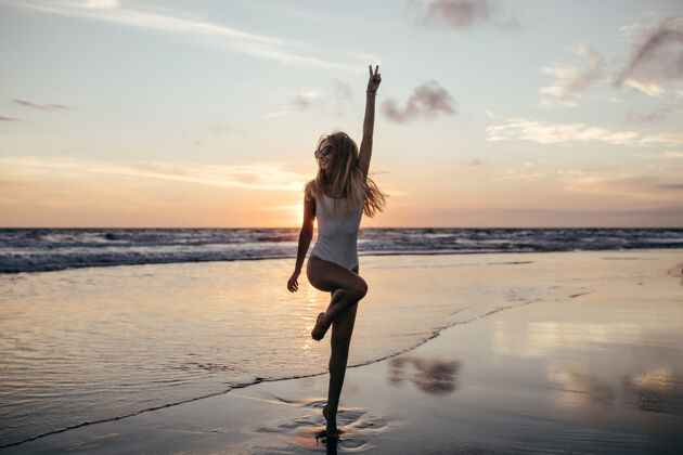 享受可爱苗条的女孩单腿站立在海边的全长镜头海洋灵感水