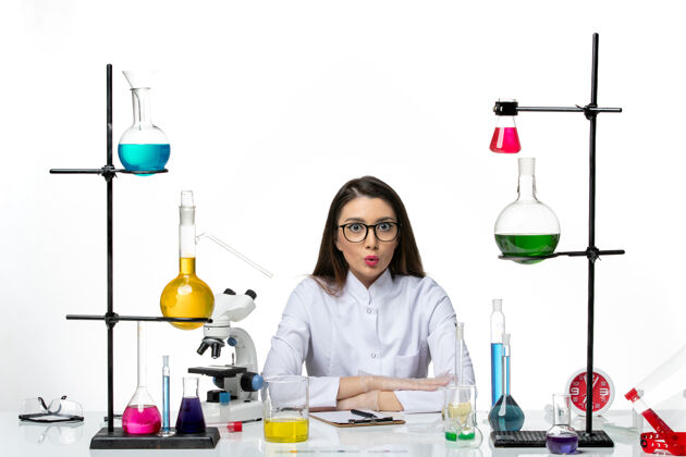 视图前视图：身着医疗服的女化学家围坐在桌子旁 拿着白色背景的解决方案实验室病毒冠状病毒大流行科学前面医疗瓶子