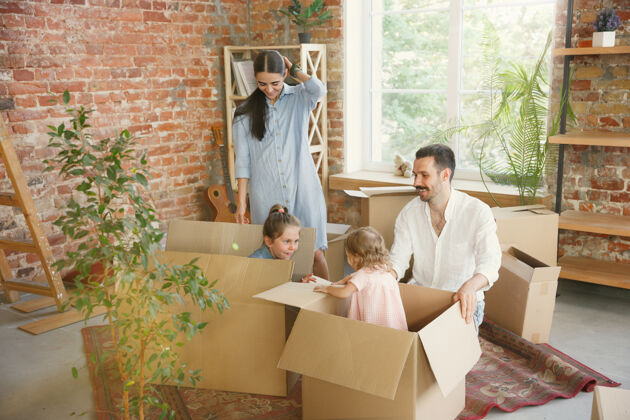 休闲新生活成年家庭搬进新房子或公寓配偶和孩子看起来快乐而自信搬家 关系 新的生活观念打开箱子和他们的东西 一起玩地板公寓纸板