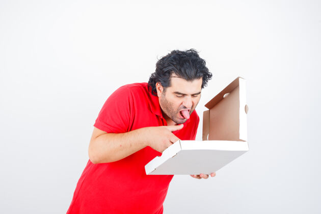 冰箱穿着红色t恤的成熟男性看着打开的比萨盒 伸出舌头 看起来很饿 正面视图营养中年的醉的
