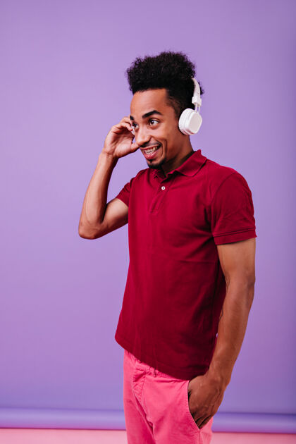 时尚体贴的非洲男人穿着红色t恤 微笑着遥望远方室内照片中的黑人男模留着滑稽的发型 戴着耳机Mp3人物耳机