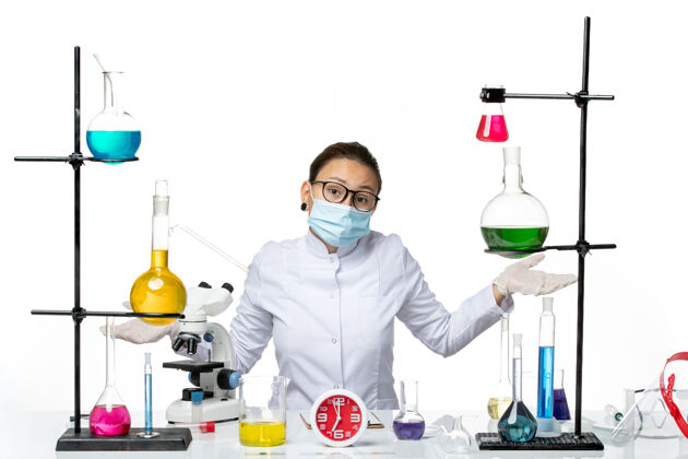坐着前视图：穿着医疗服的女化学家 戴着面罩 坐在白色背景上 化学实验室的病毒-病毒-飞溅前面医学实验室