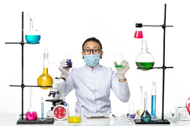 化学前视图穿着医疗服的女化学家 戴着面罩 在白色背景上拿着不同的溶液 飞溅着病毒化学实验室的covid-喷溅实验室医生