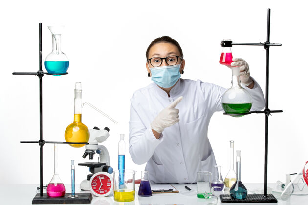 实验室正面图：穿着医疗服的女化学家 戴着面罩 在白色办公桌上工作 病毒化学实验室 covidsplash医疗外套病毒