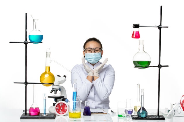 飞溅前视图穿着医疗服的女化学家带着面罩坐在桌子前面 白色背景上有解决方案病毒化学实验室的covid飞溅物解决方案科学桌子