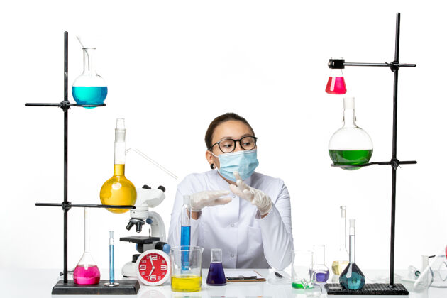 医疗前视图穿着医疗服的女化学家戴着口罩坐在房间里 桌子上放着白色背景的溶液病毒化学实验室covidsplash前面解决方案房间