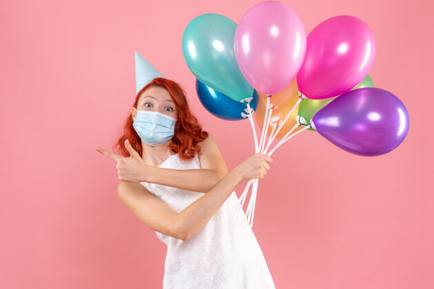 庆祝正面图年轻的女性手持彩色气球在面具上浅粉色正面乐趣节日