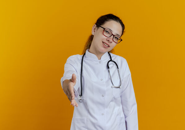 眼镜面带微笑的年轻女医生 穿着医用长袍 戴着听诊器 戴着眼镜 伸出手来女人微笑医学