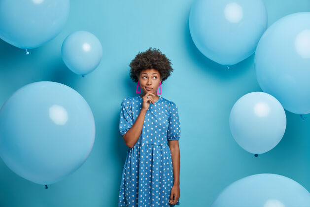 穿着体贴的黑皮肤女人穿着圆点蓝洋装 在气球派对上 穿着时髦的服装 有沉思的表情 去庆祝生日休闲时间 聚会的概念庆典非洲民族