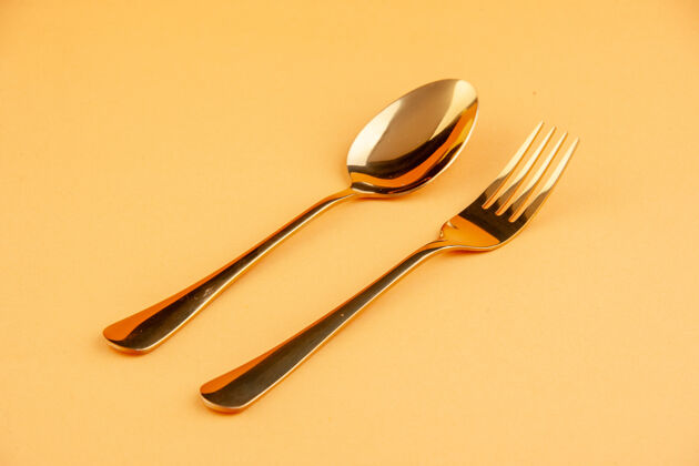 闪亮在独立的黄色背景上 近距离观看优雅闪亮的金色不锈钢勺子和叉子 空间宽敞银器午餐餐具